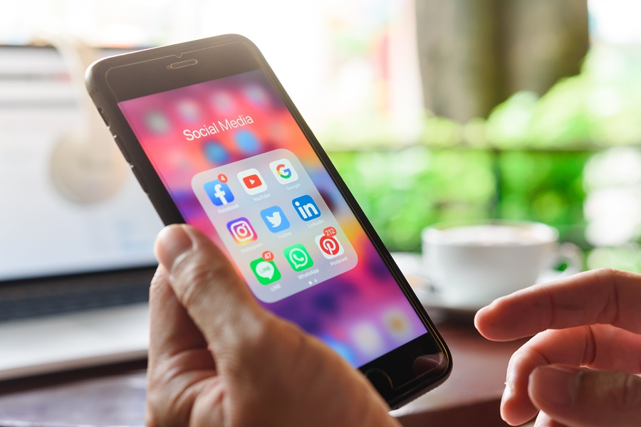 Ein Mann hält ein Smartphone in der Hand. Auf dem Smartphone sind Icons der Social Media Kanäle zu sehen